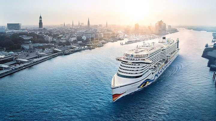 Ein Kreuzfahrtschiff von AIDA Cruises auf der Elbe in Hamburg vor der Skyline der Stadt.