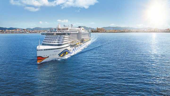 Kreuzfahrtschiff von AIDA Cruises fährt auf das sonnige Mallorca zu, im Hintergrund die Küste und die Kathedrale von Palma