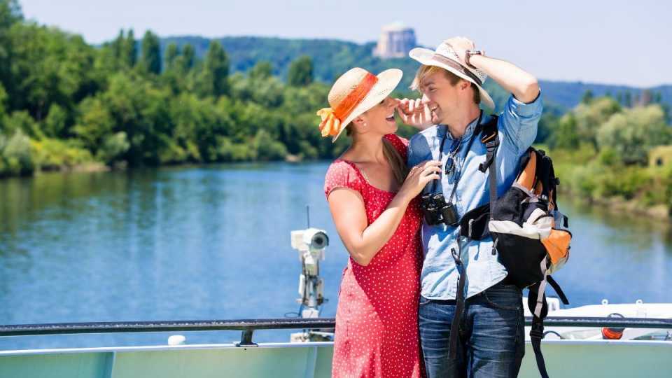 Paar genießt die Aussicht an Bord einer Flusskreuzfahrt bei sonnigem Wetter, umgeben von grünen Landschaften