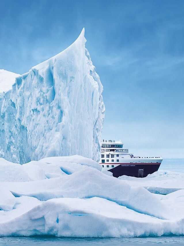 Expeditionsschiff Hanseatic Nature von Hapag-Lloyd Cruises neben einem riesigen Eisberg in der Arktis